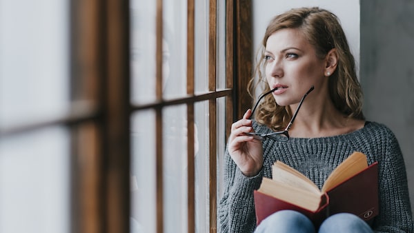 Woman sitting at the window reading and thinking