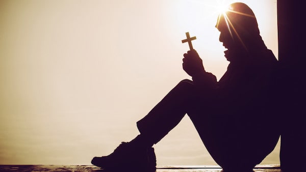 Silhouette man holding a cross in prayer