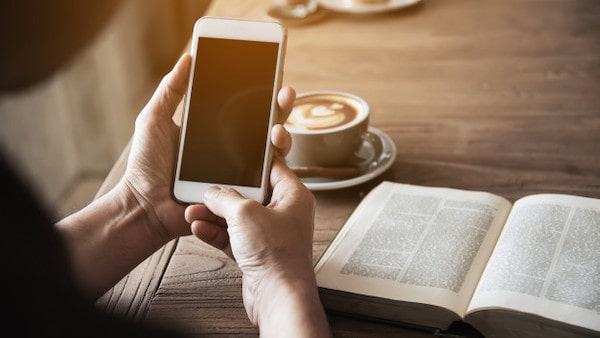 Man using mobile phone drinking coffee reading book